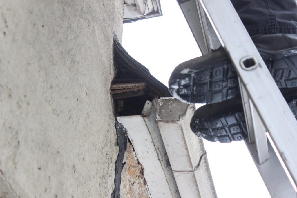 Person on ladder inspecting building exterior