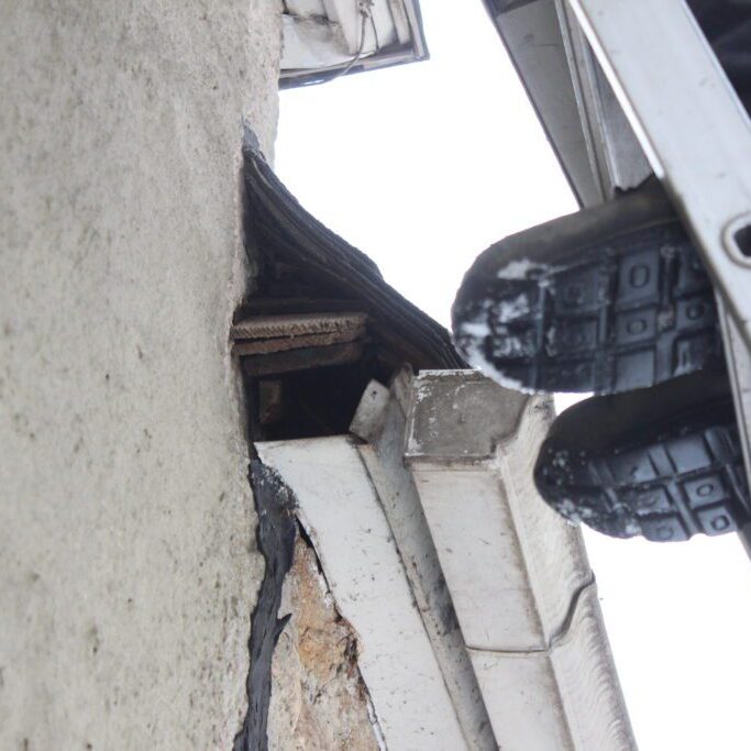 Person on ladder inspecting building exterior